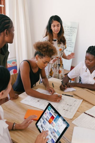 Autour d'une grande table, cinq femmes travaillent en équipe.