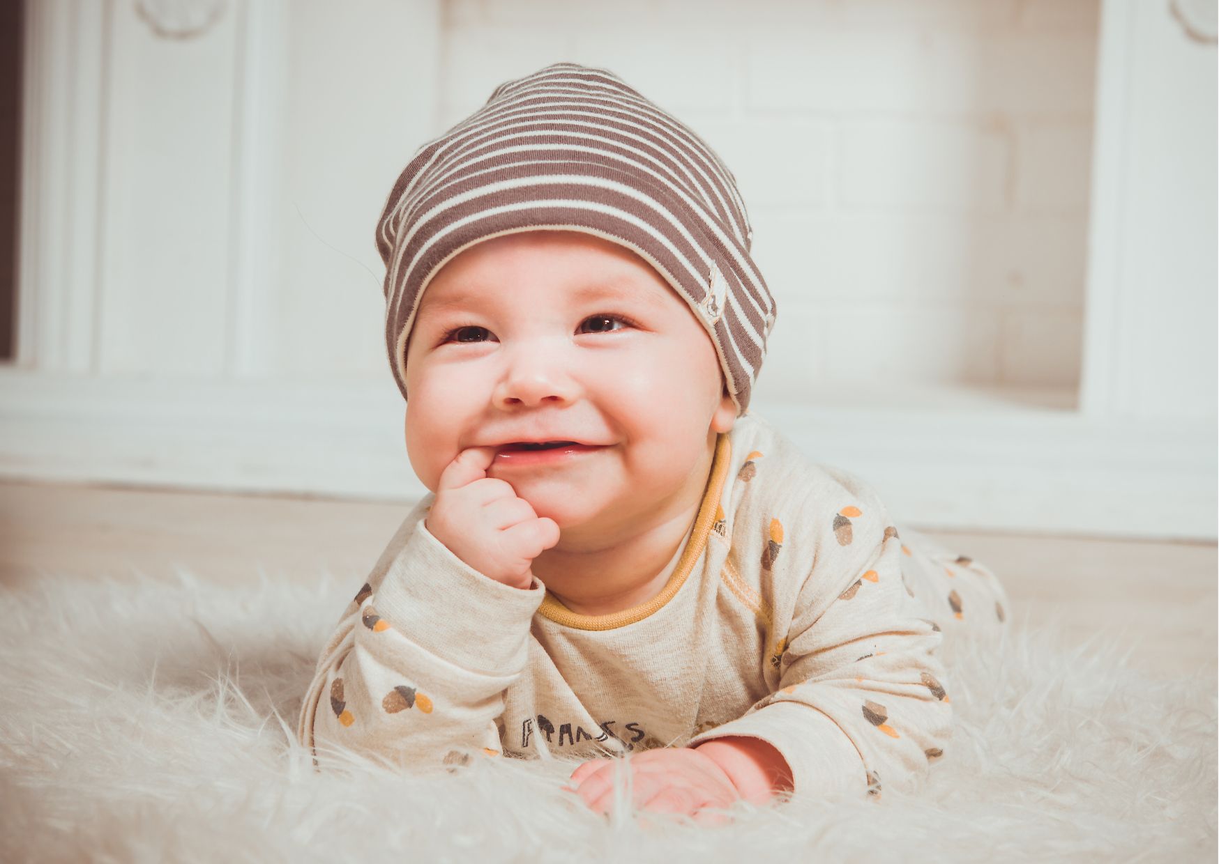 Couché sur un tapis à poils longs, bébé rit avec son doigt dans sa bouche