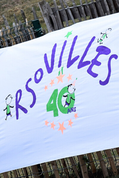 Lors de la fête d'anniversaire de l'asbl Les Arsouilles, deux personnes sourient au travers d'un ballon en forme de 40.