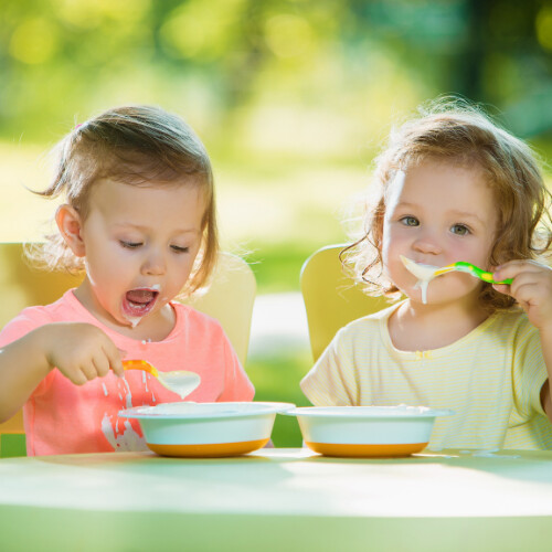 Deux petites filles assises à une table qui mange une yahourt